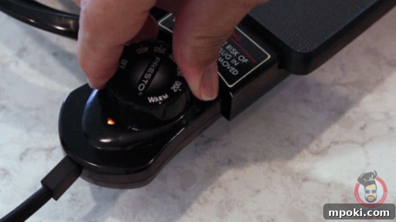 Dads Guide To Flawless French Toast 6 A hand adjusting the temperature dial on an electric griddle, highlighting precise heat control.