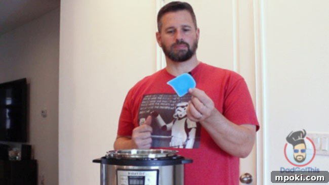 Five Best Instant Pot Secrets From a Dad 5 A hand holding a bright yellow silicone pan scraper, highlighting its non-abrasive yet effective design for cleaning cookware.