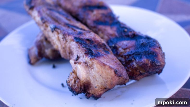 Sous Vide Spare Ribs: 12 or 24 Hours, Always Perfect 2 Sous Vide Spare Ribs on a white plate, perfectly grilled with a rich brown crust, next to a small bowl of sauce.