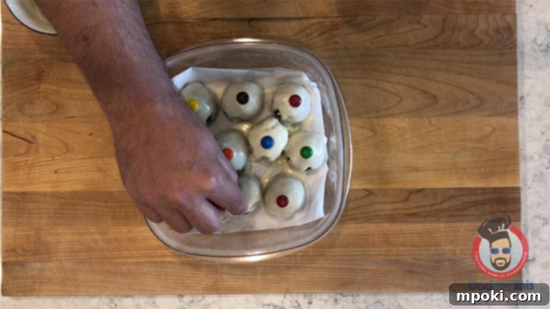 Spooktacular Oreo Truffles: Easy, Cheap, and Delicious 9 A hand placing an M&M candy on a white Oreo truffle to complete the eyeball look.