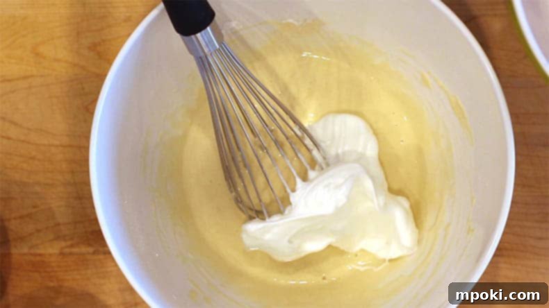 Dad Makes Amazing Japanese Pancakes 7 A whisk gently incorporating fluffy meringue into a light yellow pancake batter in a mixing bowl.