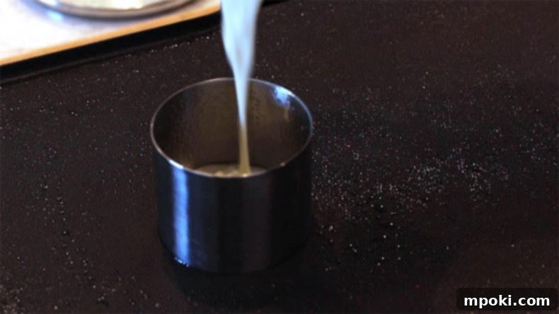 Dad Makes Amazing Japanese Pancakes 9 Pancake batter being carefully poured into a stainless steel food ring on an electric griddle.