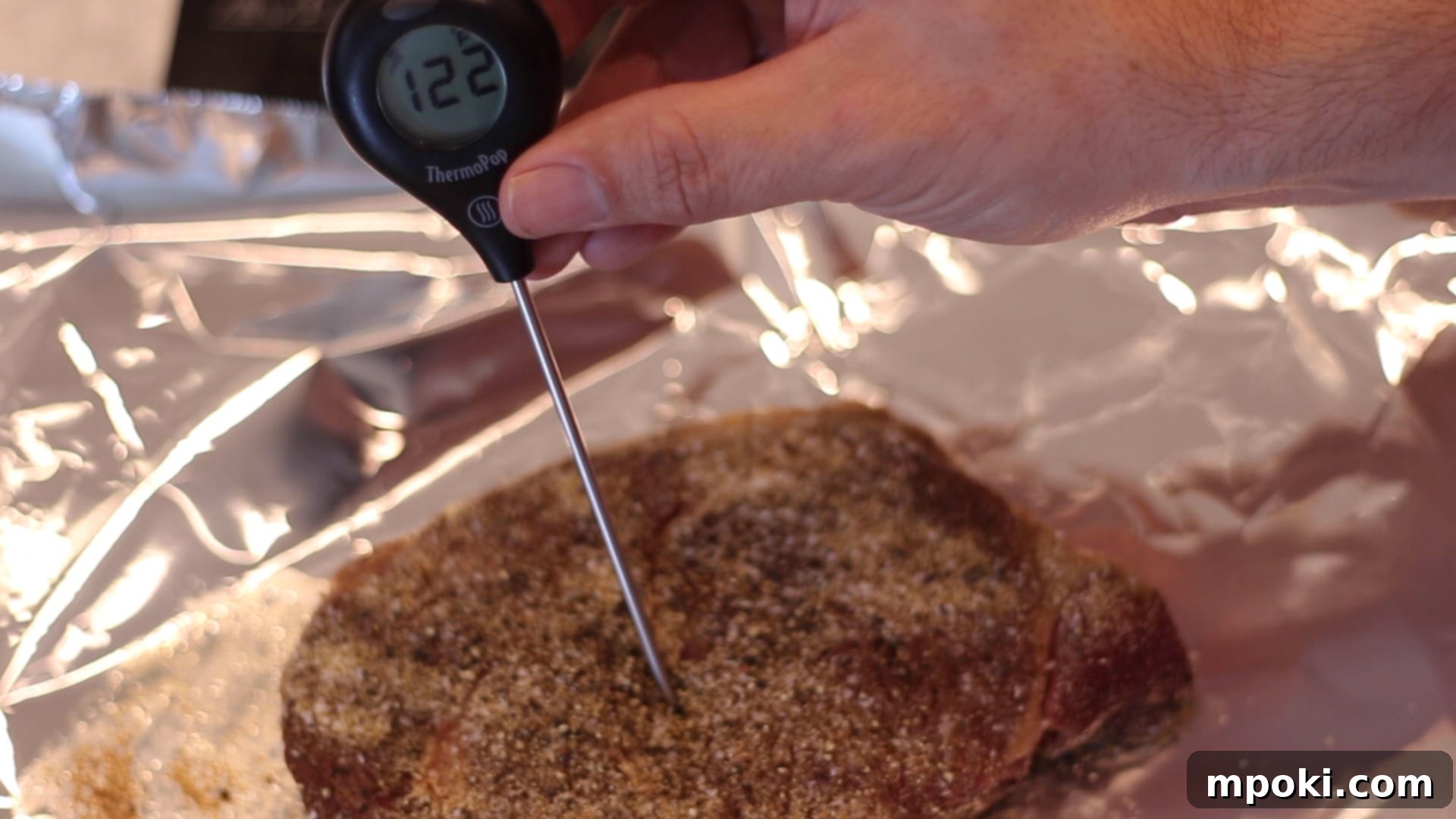 Unlocking Steak Perfection with Reverse Sear 5 A meat thermometer inserted into a steak to check its internal temperature, resting on an aluminum foil-lined baking sheet after oven cooking.