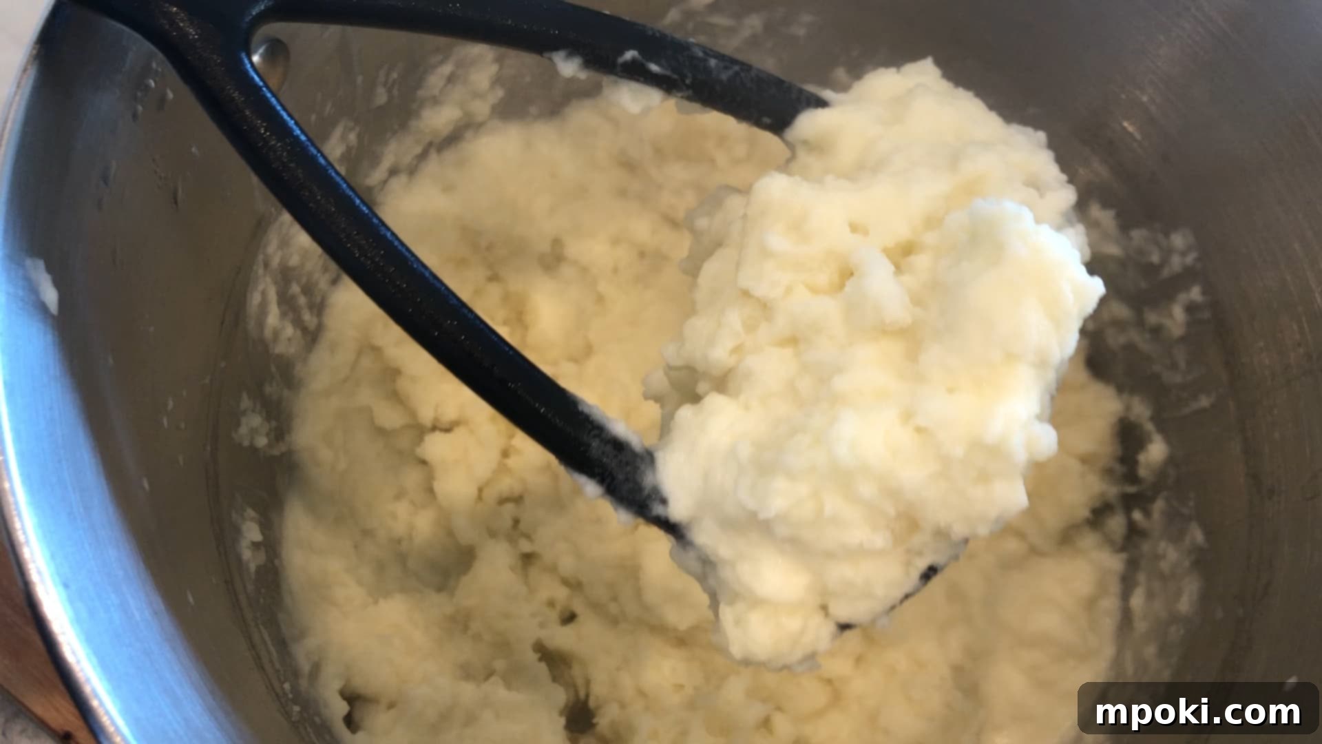 Mickey's Creamy Parmesan Mashed Potatoes 7 Drained potatoes being mashed in a pot with heavy cream and butter