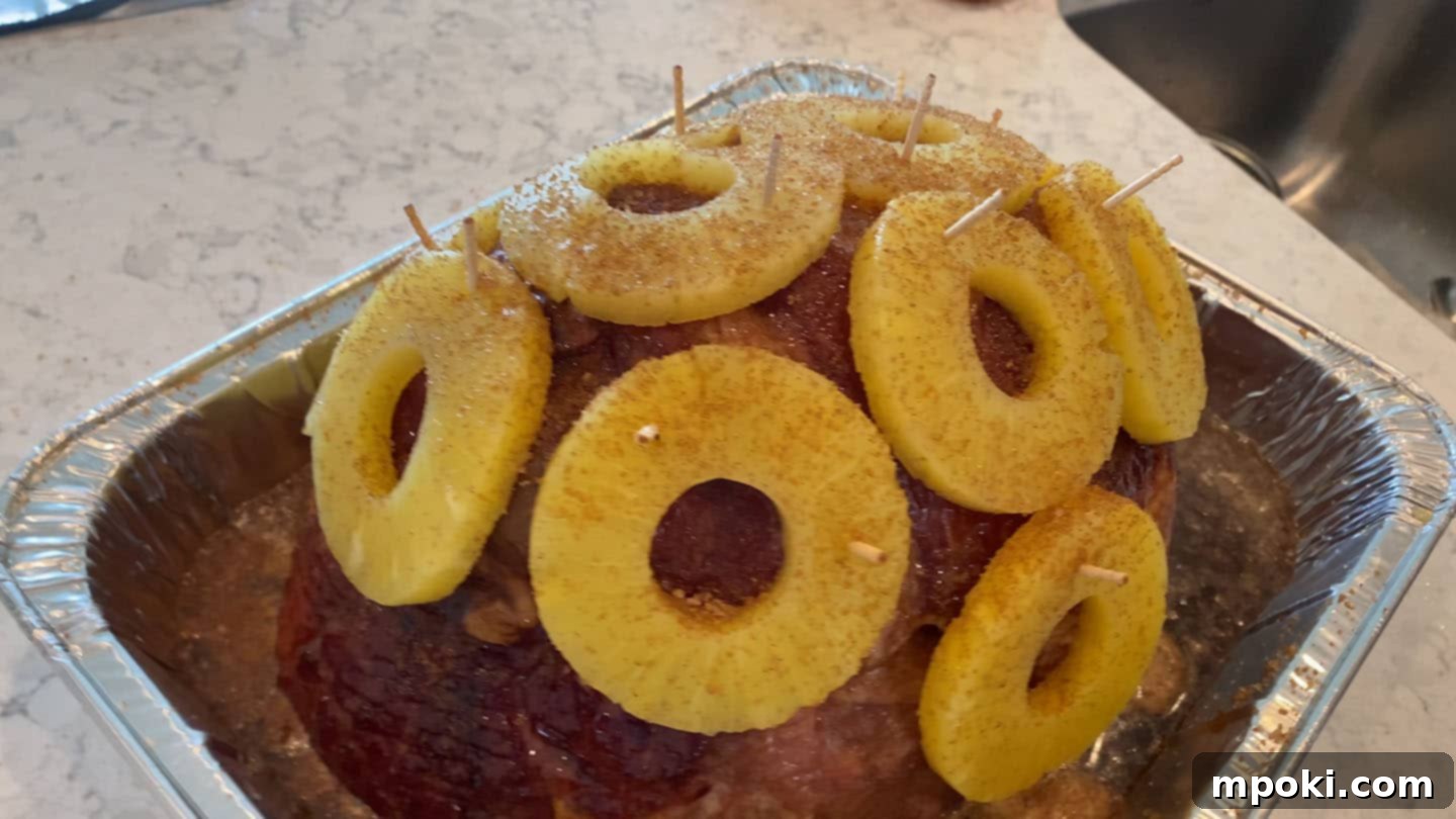 Decadent Honey Brown Sugar Glazed Spiral Ham 3 Juicy pineapple rings meticulously arranged and secured with toothpicks atop a spiral sliced ham, ready for glazing and baking.