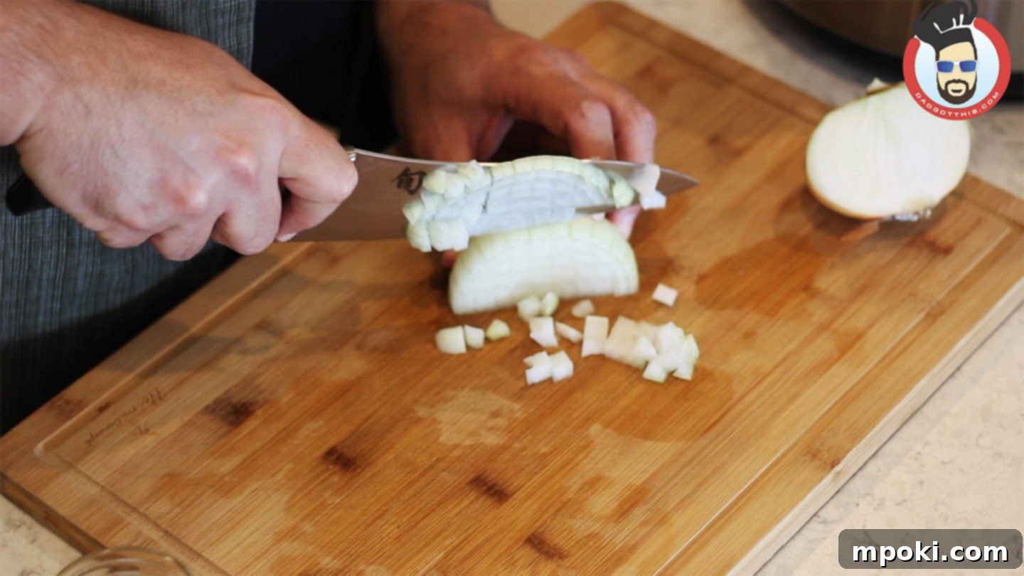 Hearty Instant Pot Zuppa Toscana 4 Hands dicing a white onion finely on a cutting board, preparing it for the Zuppa Toscana recipe.